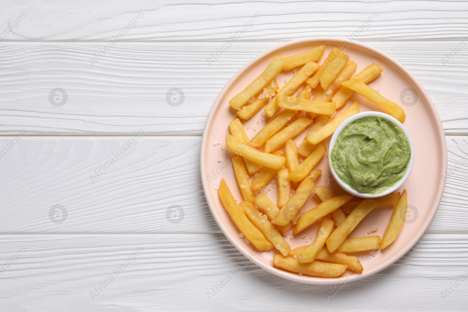 Photo of Plate with french fries and avocado dip on white wooden table, top view. Space for text