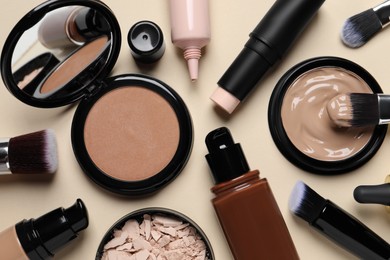 Liquid foundations, beauty accessories and face powders on beige background, flat lay