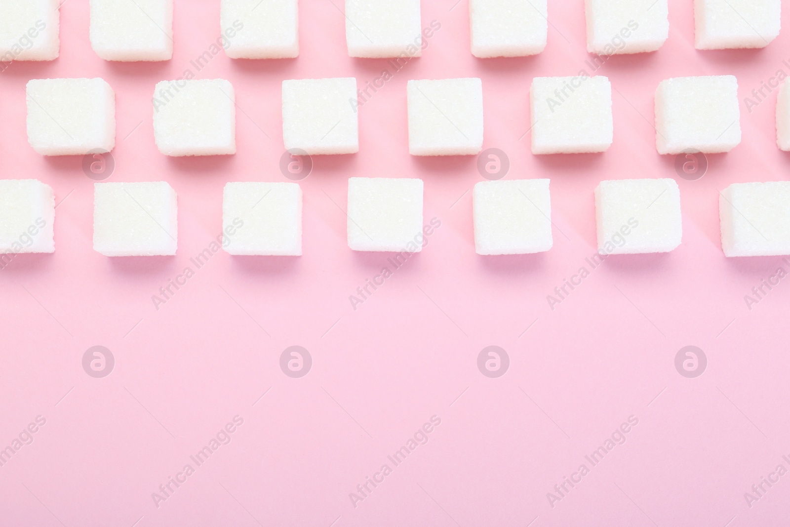 Photo of White sugar cubes on pink background, top view. Space for text