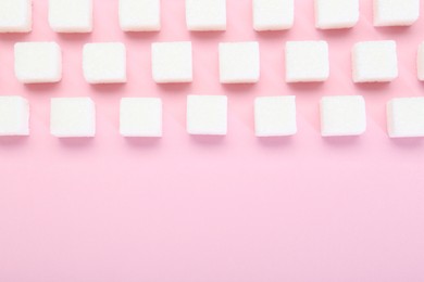 White sugar cubes on pink background, top view. Space for text
