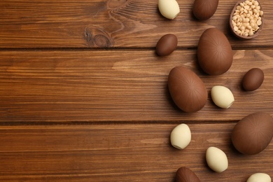 Photo of Sweet chocolate eggs and candies on wooden table, flat lay. Space for text