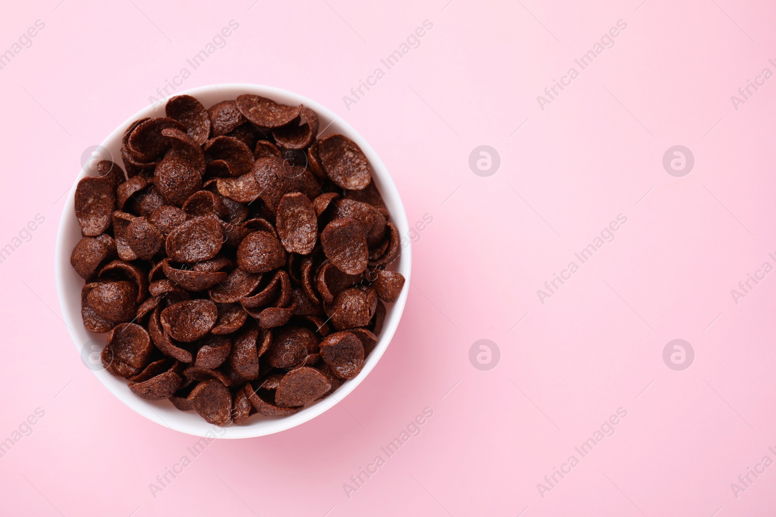 Photo of Breakfast cereal. Chocolate corn flakes in bowl on pink table, top view. Space for text