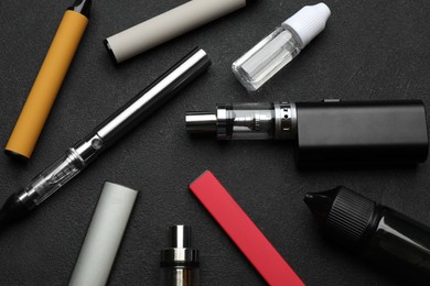 Photo of Different electronic cigarettes on black table, flat lay. Smoking alternative