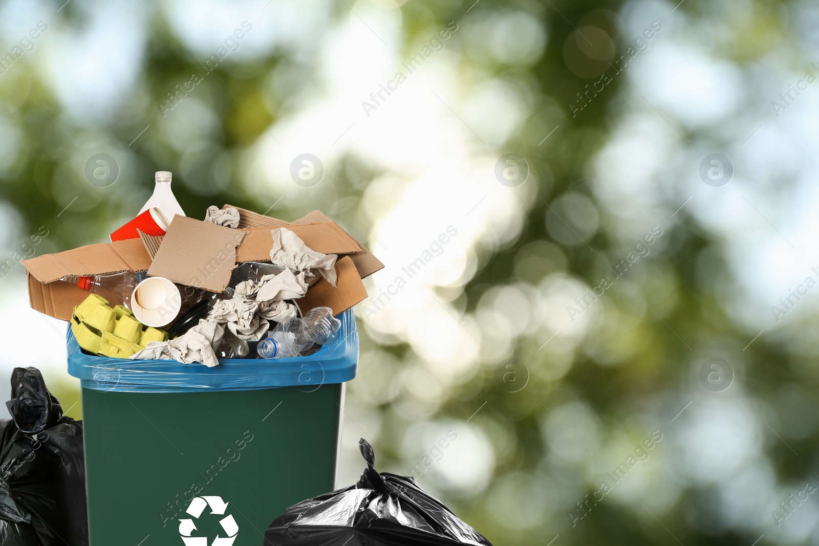 Image of Waste bin and plastic bags full of garbage on blurred background, space for text