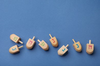Wooden dreidels on blue background, flat lay with space for text. Traditional Hanukkah game