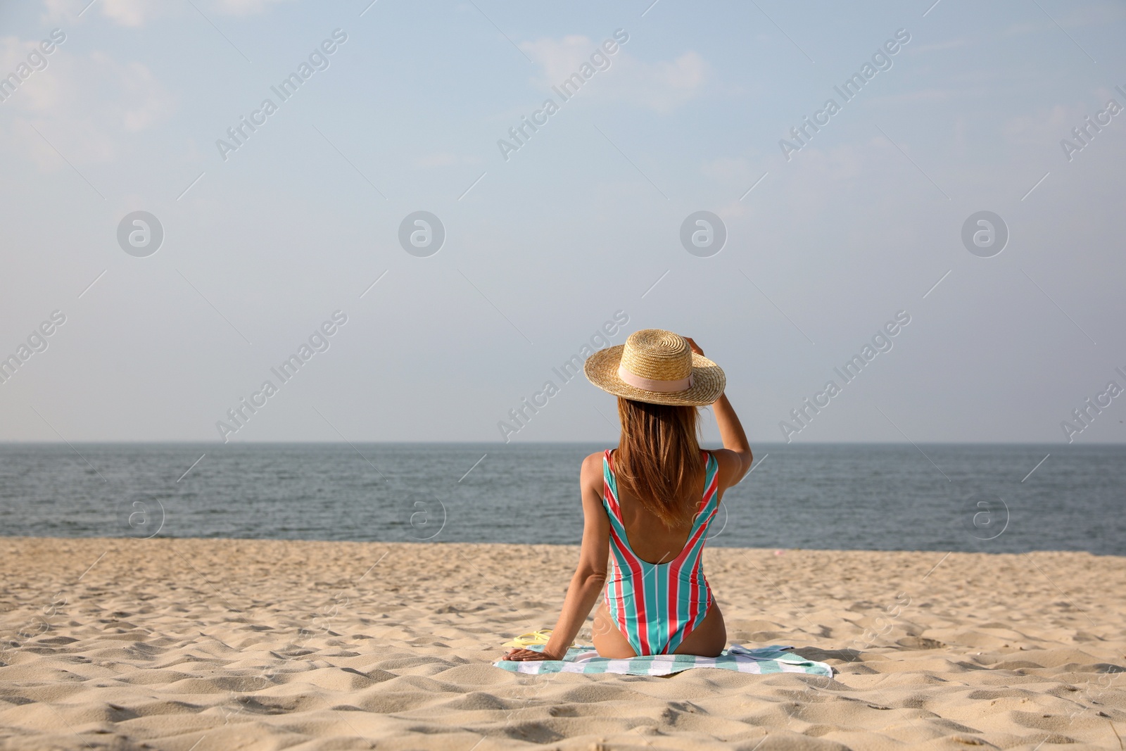 Photo of Woman with beach towel resting on sandy seashore, back view. Space for text