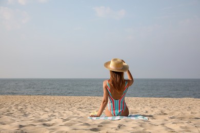 Woman with beach towel resting on sandy seashore, back view. Space for text