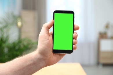 Image of Man holding smartphone with green screen indoors, closeup. Gadget display with chroma key. Mockup for design