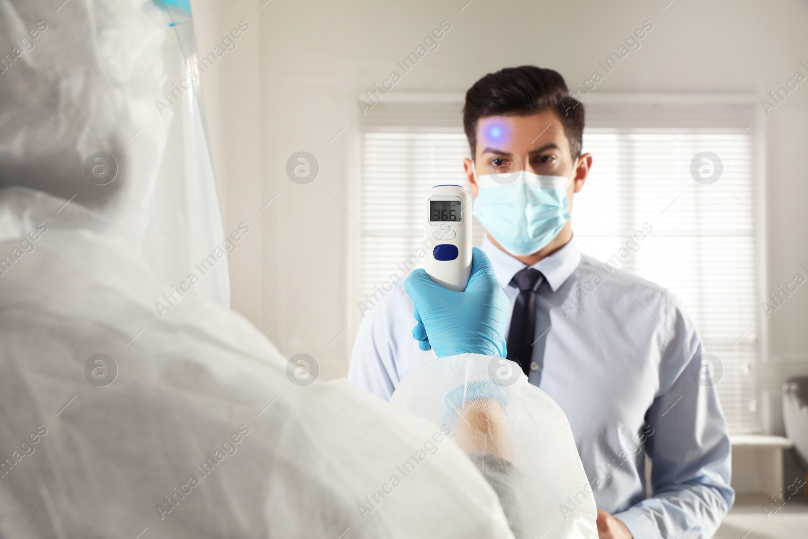 Image of Doctor measuring man's temperature in office closeup. Prevent spreading of Covid-19