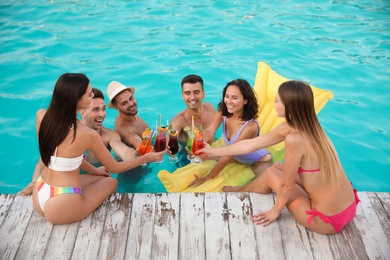 Happy young friends with refreshing cocktails enjoying pool party