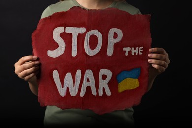 Photo of Woman holding poster with words Stop the War on black background, closeup