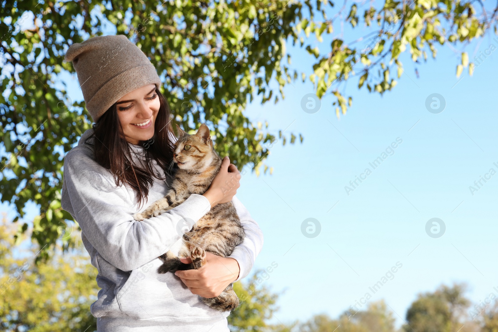 Photo of Young woman with cute stray cat outdoors. Space for text