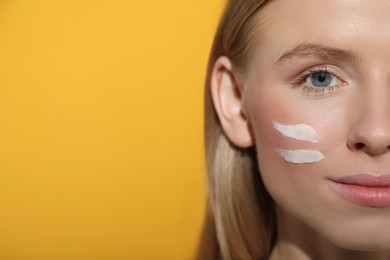 Beautiful young woman with sun protection cream on her face against orange background, closeup. Space for text