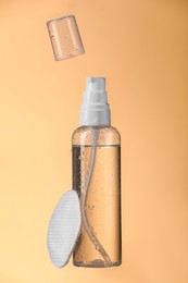 Photo of Wet bottle with micellar water and cotton pad on pale orange background