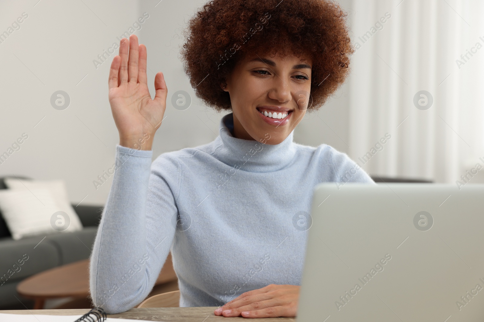 Photo of Beautiful young woman having video chat via laptop and saying hello at wooden desk in room