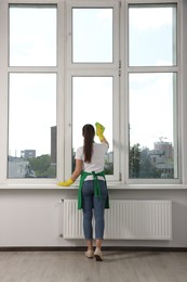 Photo of Woman cleaning window glass with cloth indoors, back view