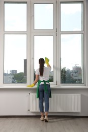 Woman cleaning window glass with cloth indoors, back view