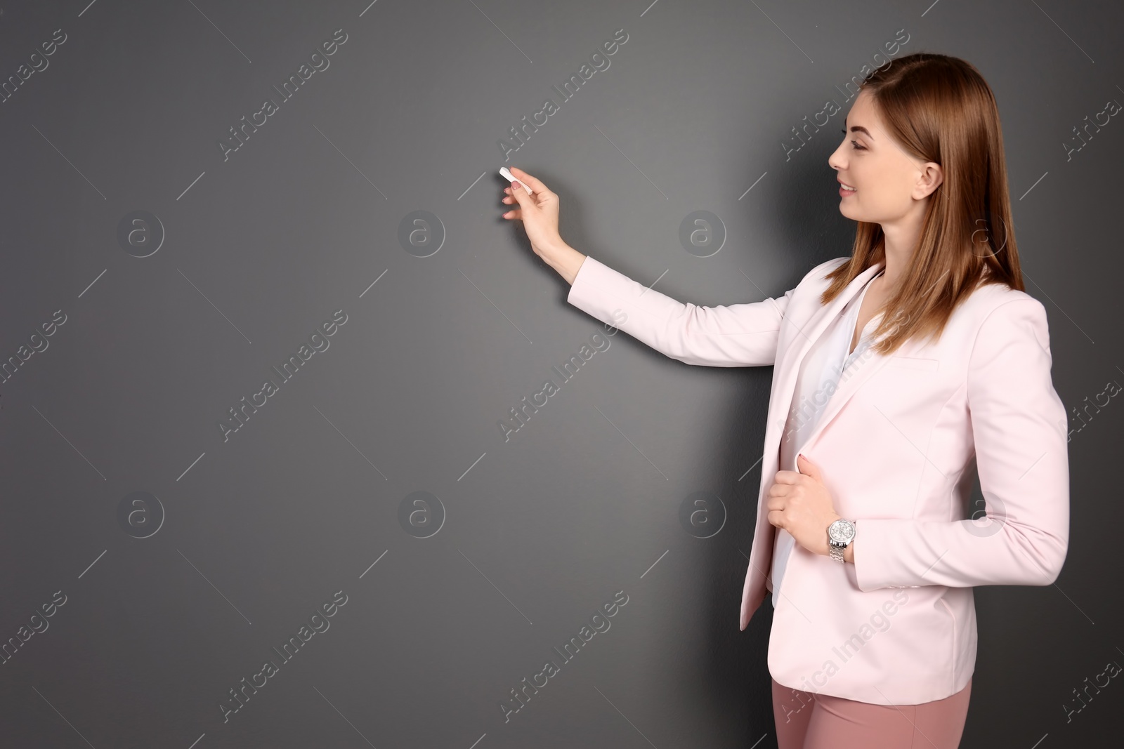 Photo of Beautiful young teacher with chalk on grey background