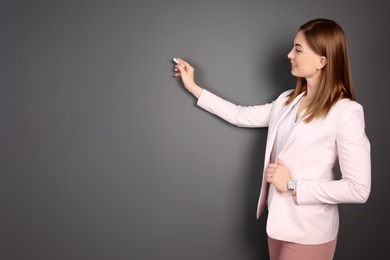 Photo of Beautiful young teacher with chalk on grey background