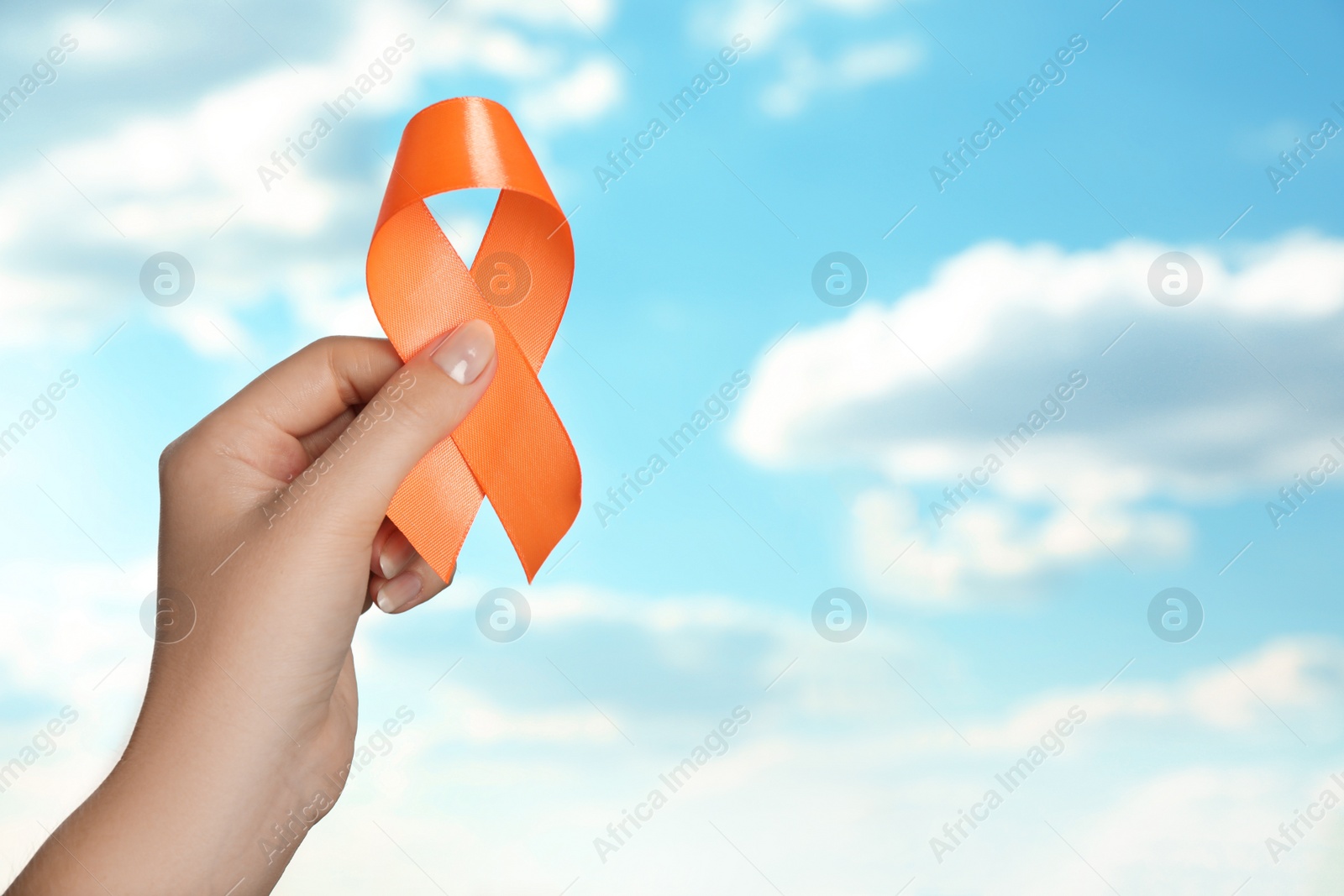 Photo of Woman holding orange ribbon against blue sky, closeup with space for text. Multiple sclerosis awareness