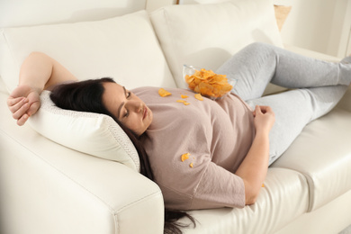 Photo of Lazy overweight woman with chips resting on sofa at home