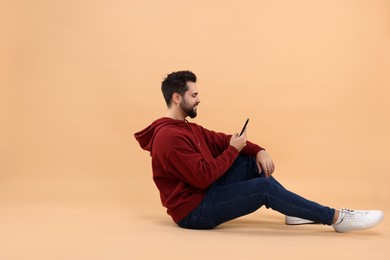 Photo of Handsome young man using smartphone on beige background, space for text