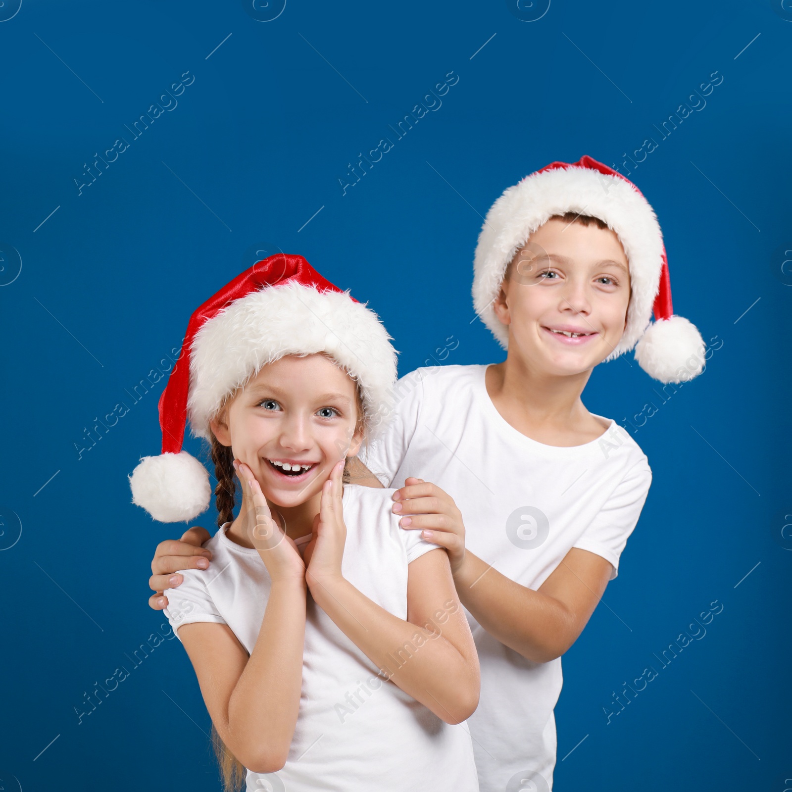 Image of Happy little children in Santa hats on blue background. Christmas celebration