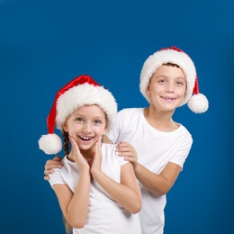 Image of Happy little children in Santa hats on blue background. Christmas celebration