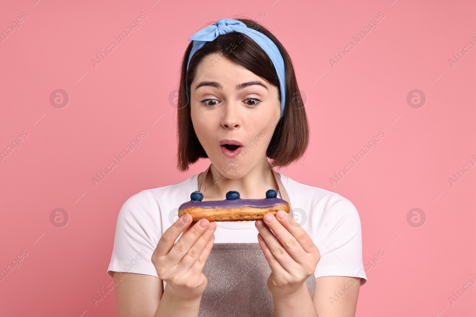 Photo of Confectioner with delicious eclair on pink background