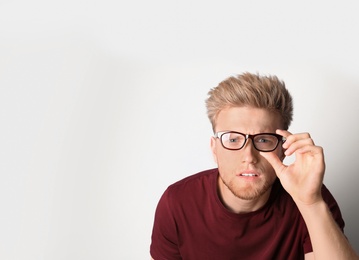 Young man with vision problem wearing glasses on light background