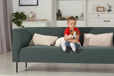 Little boy with his cute dog on sofa at home, space for text. Adorable pet
