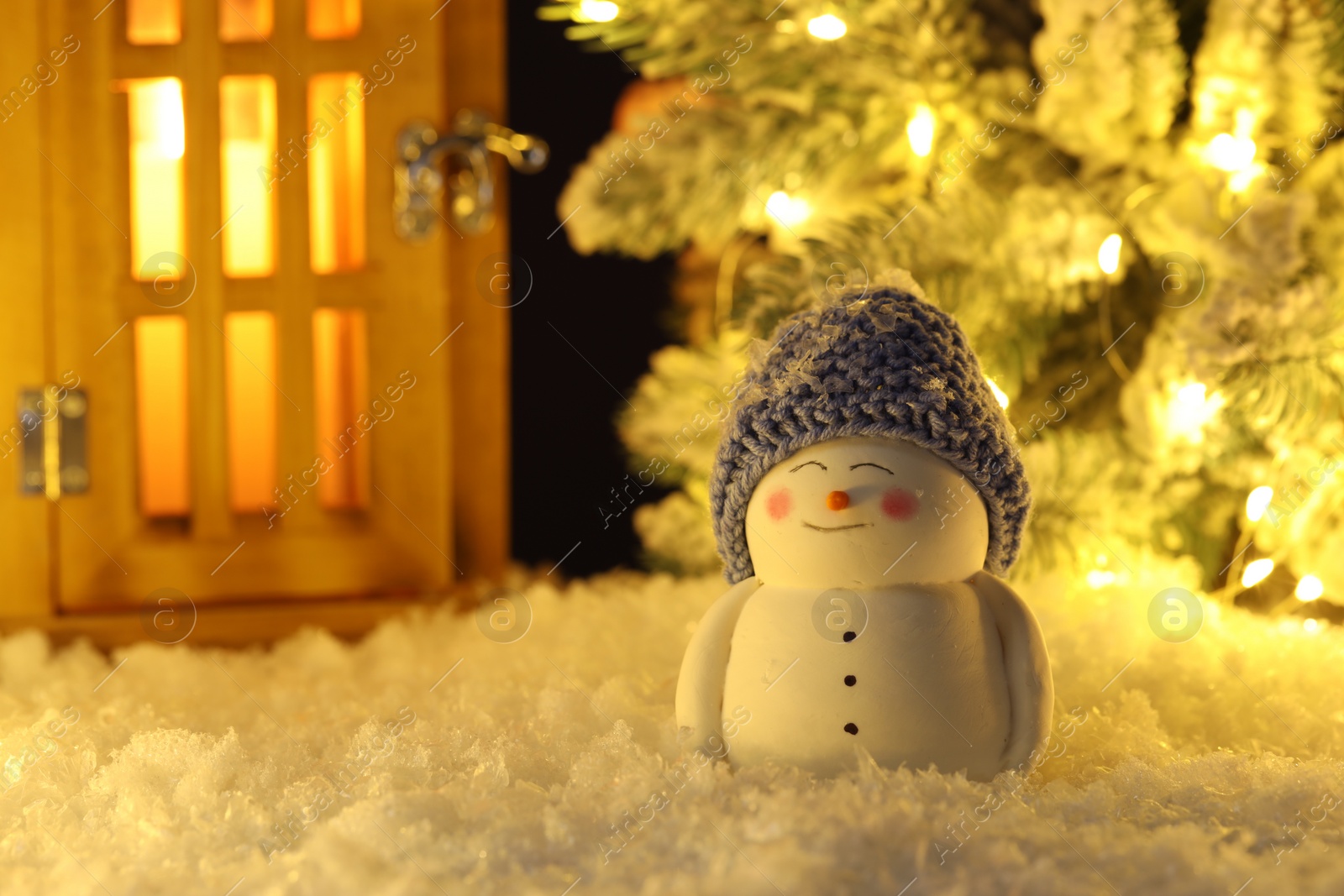 Photo of Cute decorative snowman, lantern and Christmas tree on artificial snow
