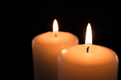 Photo of Wax candles burning on black background, closeup