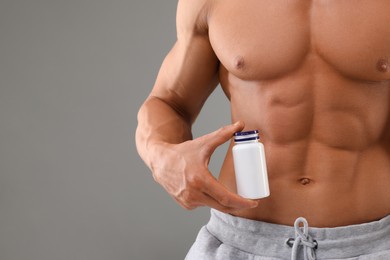Photo of Weight loss. Athletic man with bottle of supplements on grey background, closeup. Space for text