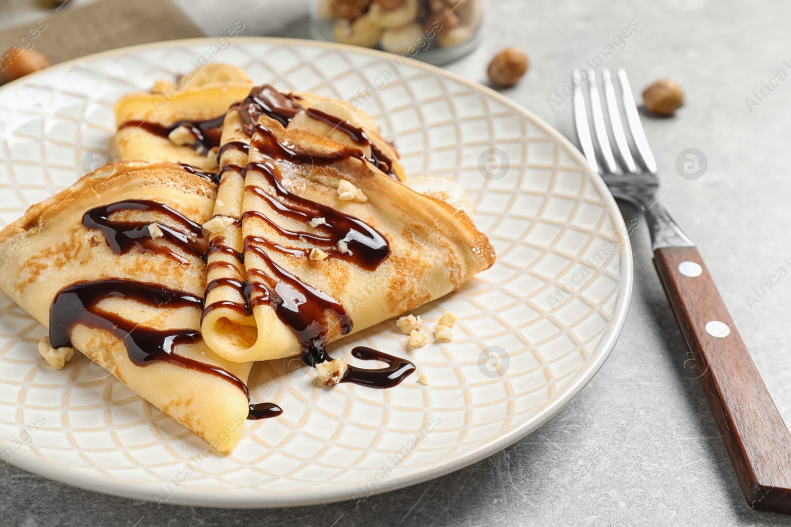 Photo of Delicious thin pancakes with chocolate spread, banana and nuts on table, closeup