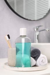 Bottle of mouthwash, toothbrushes and towels on white table in bathroom