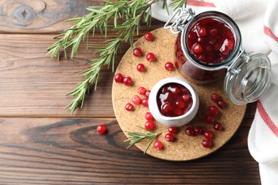 Photo of Cranberry sauce, fresh berries and rosemary on wooden table, flat lay