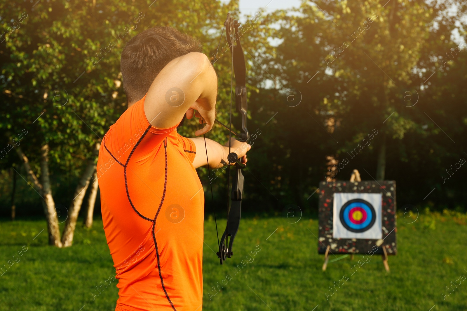 Photo of Man with bow and arrow aiming at archery target in park, back view