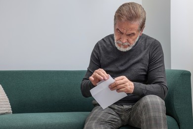 Upset senior man holding envelope and photo on sofa at home. Loneliness concept