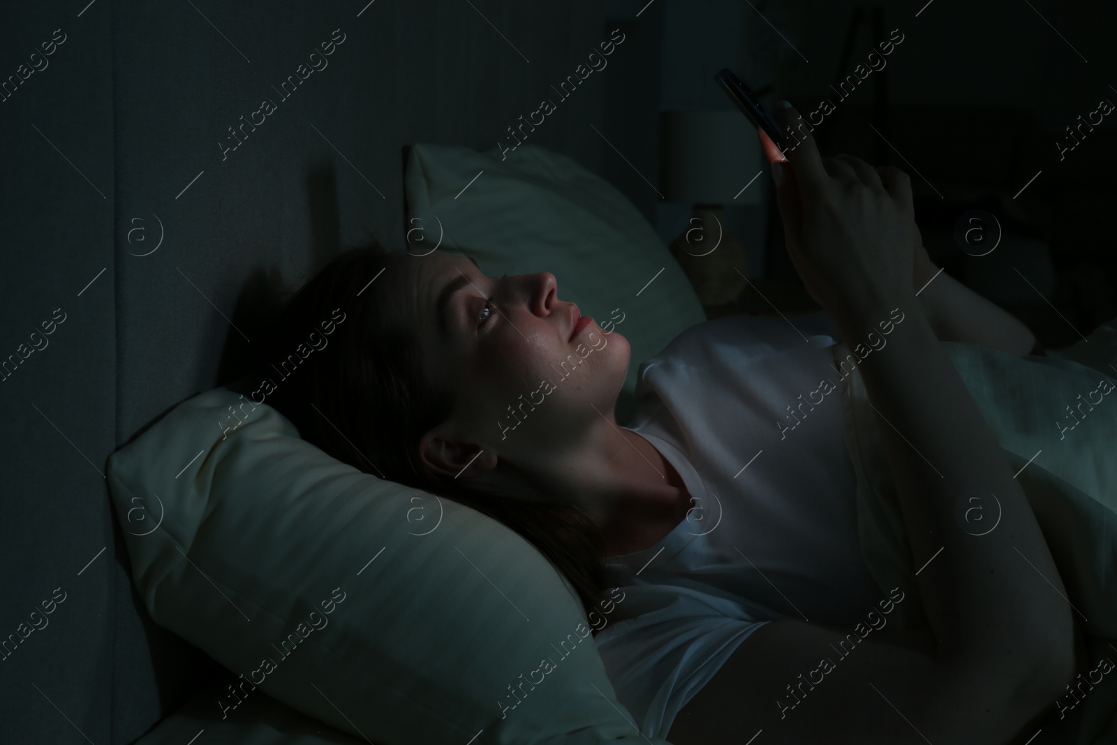 Photo of Woman using smartphone on bed at night. Internet addiction