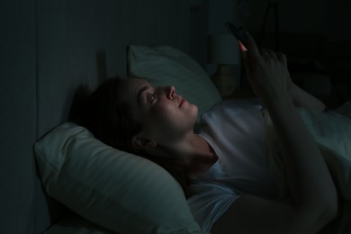 Photo of Woman using smartphone on bed at night. Internet addiction