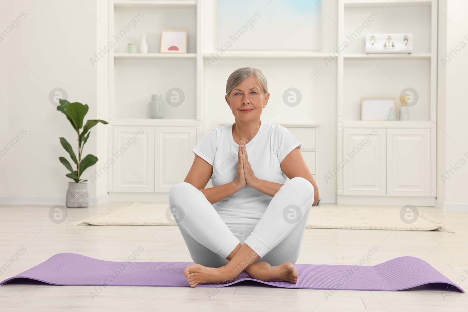 Photo of Senior woman practicing yoga on mat at home