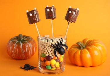 Delicious candies decorated as monsters on orange background. Halloween treat