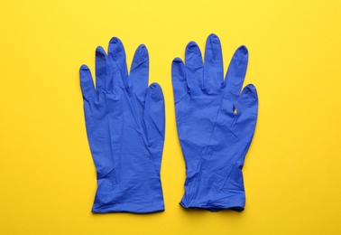 Photo of Pair of medical gloves on yellow background, flat lay