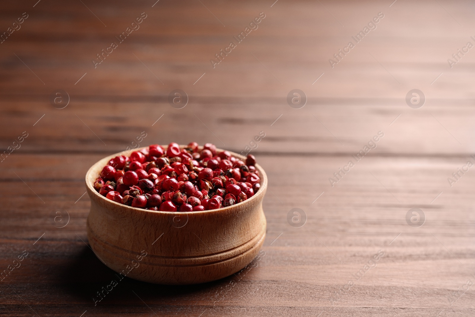 Photo of Bowl of red pepper corns on wooden table, space for text