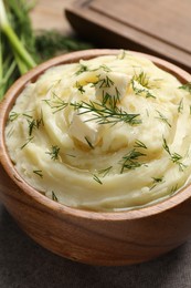 Bowl of delicious mashed potato with dill and butter on grey tablecloth, closeup