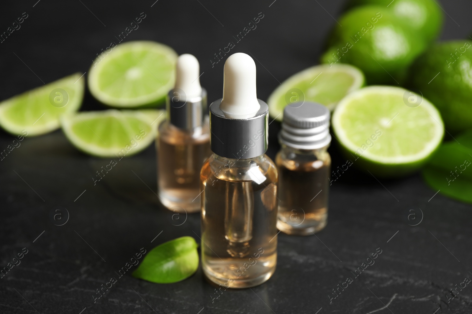 Photo of Lime essential oil and cut citrus fruits on black table