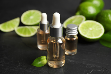 Photo of Lime essential oil and cut citrus fruits on black table