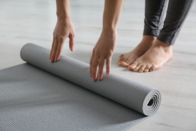 Photo of Woman rolling yoga mat on floor indoors, closeup