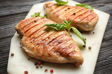 Photo of Tasty grilled chicken fillets with peppercorns and green basil on white marble board, closeup